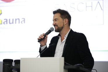 Ein Mann redet durch ein Mikrofon zum Publikum