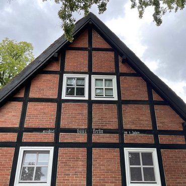 Ein dunkelrotes Fachwerkhaus in Alt-Rehse mit weißen Fensterrahmen und blauem Himmel.