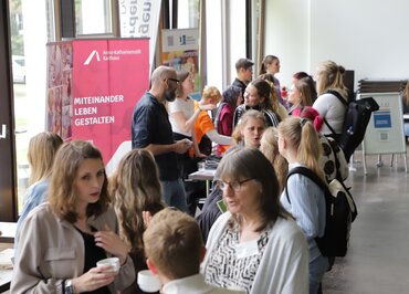 Junge Menschen stehen in Gruppen beisammen und unterhalten sich. Im Hintergrund stehen roll-ups, die für Praxiseinrichtungen werben.