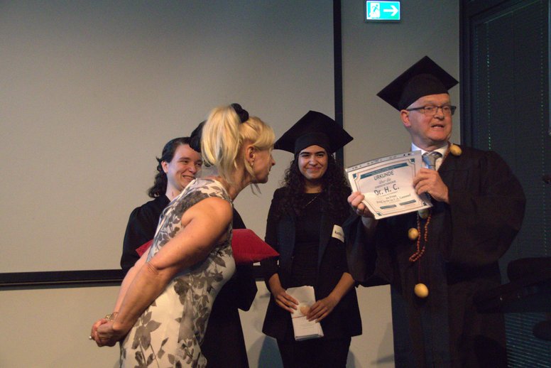Christof Stock mit Doktorhut und Kutte überreicht Antonia Lammel eine Urkunde.