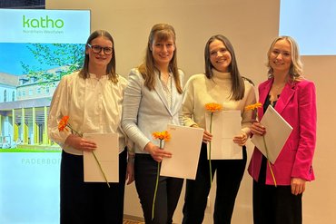 Vier Personen halten ihre Graduiertenschreiben und Urkunden in der Hand. Sie sind glücklich.