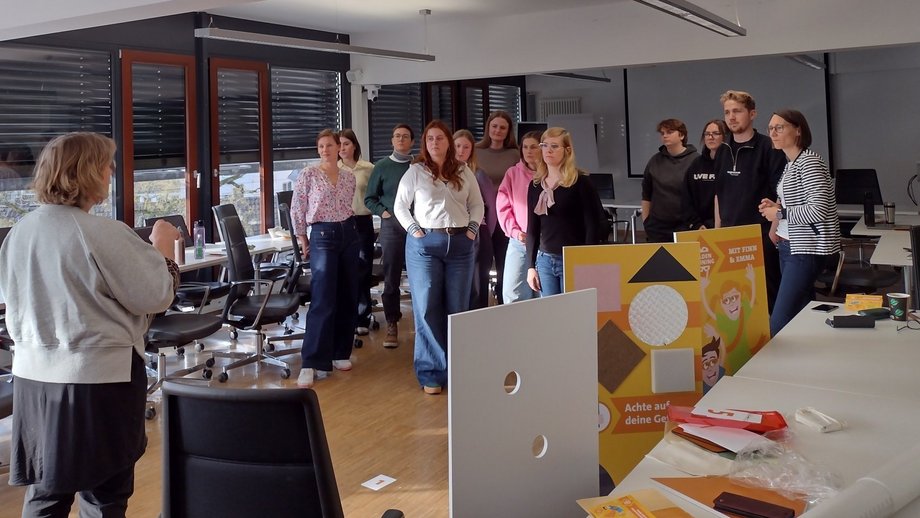 Eine Trainerin steht im Raum und ihr gegenüber stehen die Schulungsteilnehmenden.