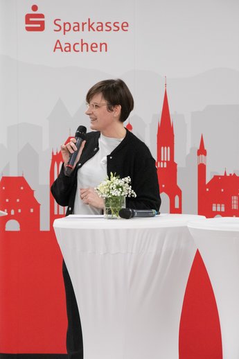 Sabine Bausch steht mit einem Mikrofon am Stehtisch