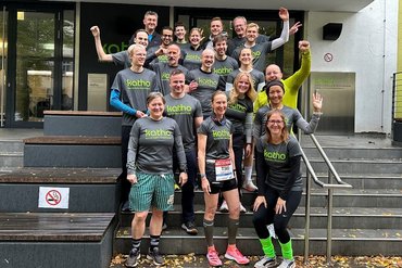 Eine Gruppe von 20 katho-Angehörigen in grauen Laufshirts vor dem Haupteingang der katho in Köln.