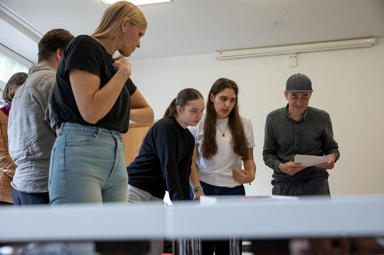 Mehrere Personen stehen an einen Tisch und schauen auf Papiere.