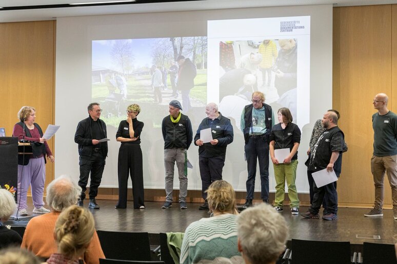 Einige Menschen stehen auf dem Podium vor einer Präsentation.