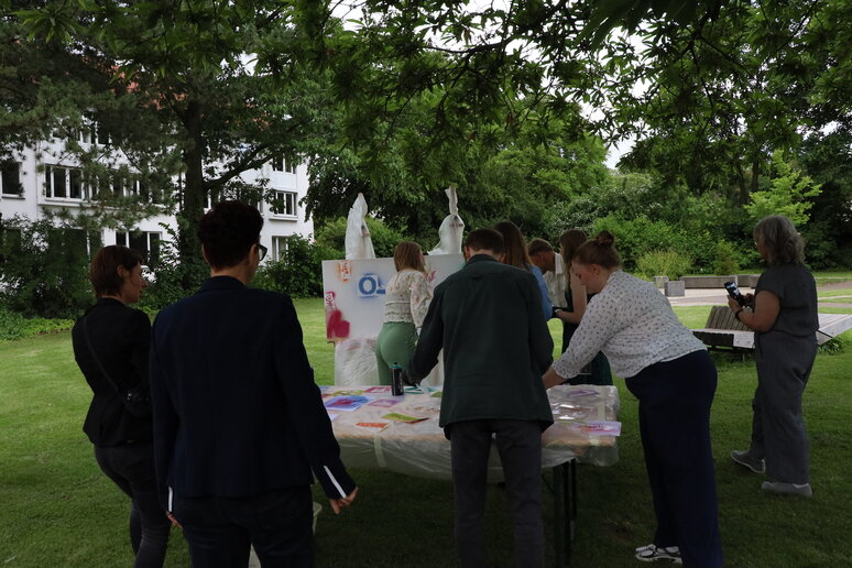 Die Absolvent_innen stehen im Garten und gestalten eine Leinwand mit Grafitti