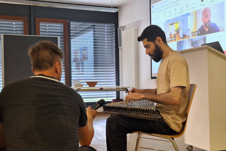 Ein Mann spielt sitzend auf einem zitherähnlichen Instrument. Neben ihm hält jemand ein Mikrofon.