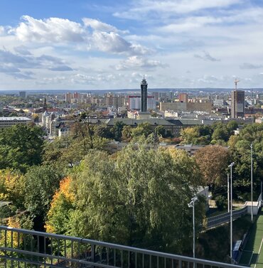 Blick über die herbstliche Stadtlandschaft von Ostrava in Tschechien mit grünen Baumflächen, Stadtsilhouette und blauem Himmel.