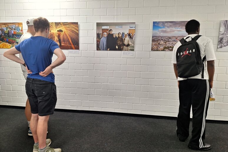 Drei junge Männer betrachten großformatige Fotos an einer Wand. Das mittlere Foto zeigt fünf Frauen, die Kopftuch tragen.