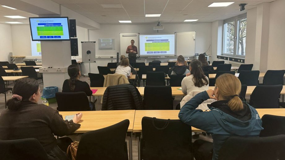 Prof. Dr. Brühe steht vorne, im Hintergrund sitzen zuhörende Studierende und Interessierte.
