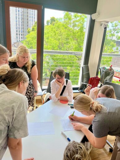 Auf Bild sind verschiedene Studierende und Prof.in Dr. Anette Müller, die mehre Projekte begleitet sind. Gemeinsam schreiben sie etwas auf.