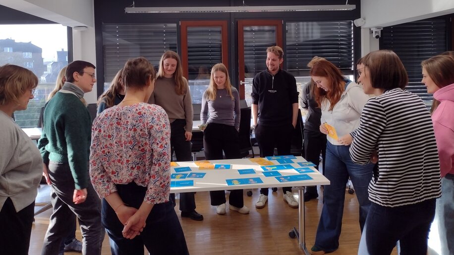 Die Schulungsteilnehmenden sichten das Schulungsmaterial an einem Tisch stehend.