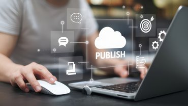 Ein Mann sitzt vor seinem Laptop am Schreibtisch. Über der Tastatur des Laptops sind verschiedene Symbole zu sehen. In der Mitte ist eine Wolke mit dem Text: Publish. 