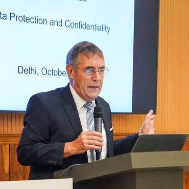Professor Jox steht mit Mikro in der Hand an einem Redepult. Hinter ihm eine Präsentation, auf der die Worte "Protection and Confidentiality" sowie "Delhi".