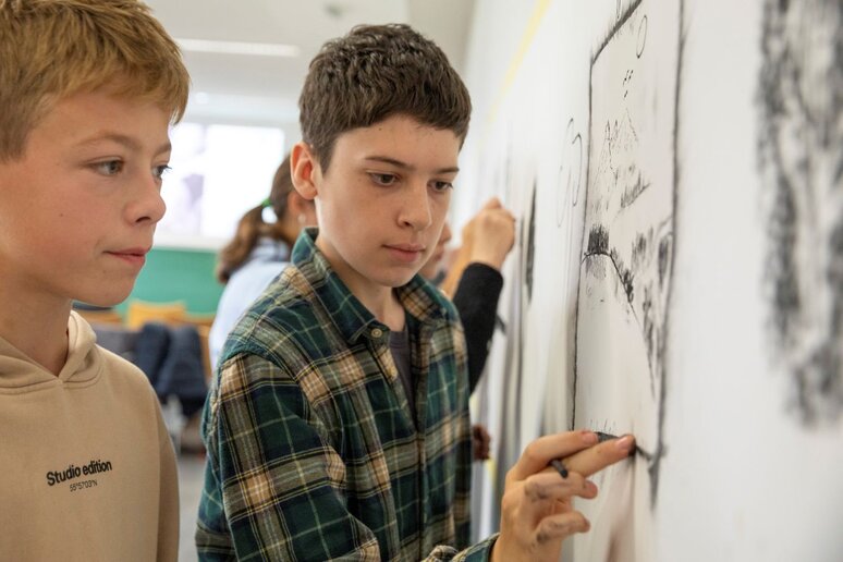 Schüler:innen malen mit Kohle auf an der Wand befestigtem Papier.