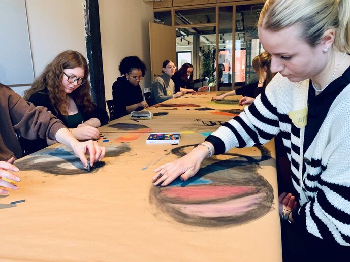 Schüler:innen sitzen an einen Tisch und gestalten Bilder.