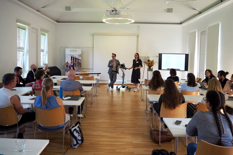 Teilnehmende sitzen an Tischreihen im Seminarraum. Vor Kopf stehen Professor Laukötter und Professorin Panreck.