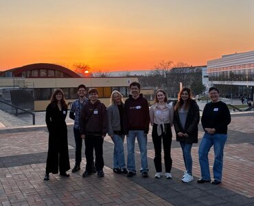 Gruppenfoto der Seminarleiterinnen Prof.in Dr.in Katharina Motzke und Dr.in Teresa Frank mit den Studierenden des Kooperationsseminars im Freien vor einem Sonnenuntergang.