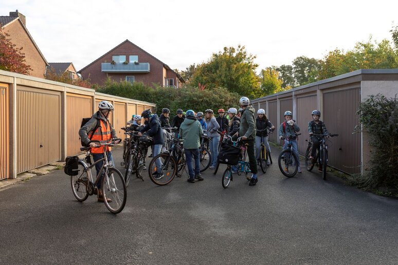 Eine Gruppe Schüler:innen steht mit ihren Fahrrädern zwischen Garagen.