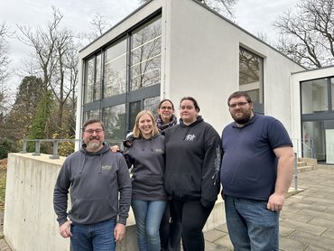 Fünf Tutor_innstne stehen in einer Gruppe draußen zusammen.