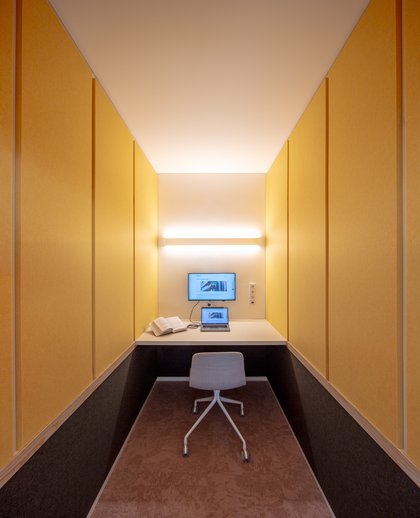 Eine Lernkabine von innen mit gelben Wänden und rosefarbigen Teppich sowie Monitor und Schreibtisch