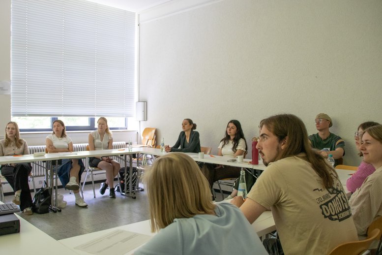 Tagungsteilnehmende sitzen in einem Seminarraum an Tischen und diskutieren.