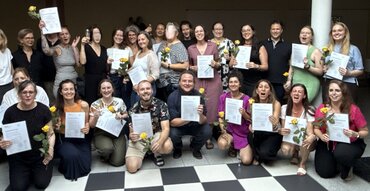 24 Personen halten ihre Zertifikate hoch. Sie lächeln und freuen sich. 