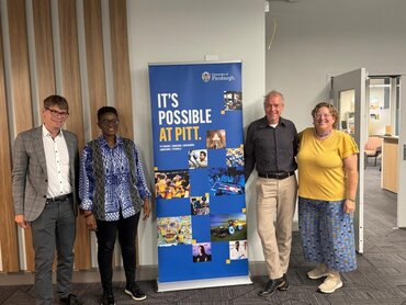 Vier Personen stehen neben einem Roll-up mit der Aufschrift "It's possible at PITT".