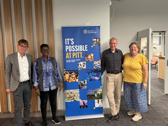Vier Personen stehen neben einem Roll-up mit der Aufschrift "It's possible at PITT".