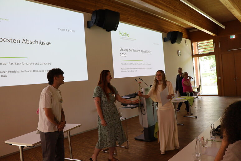 Einer Absolventin wird das Zeugnis von Prof.in Dr.in Julia Höke und Prof. Dr. Christoph Blomberg und eine Blume von einer Studentin des AStA überreicht. 