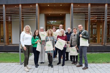 Zehn Alumni stehen vor dem Gebäude der katho am Standort Paderborn. Sie tragen einen jutebeutel mit der Aufschrift "wertvoll" und lächeln freundlich in die Kamera.
