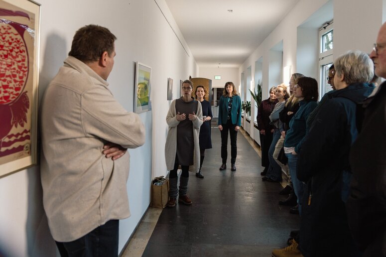 Eine Dozierende erläutert ihr Bild: Malerei (Gouache) in gelb und blau/grün.