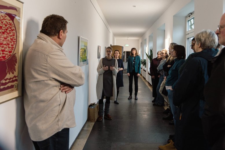 Eine Dozierende erläutert ihr Bild: Malerei (Gouache) in gelb und blau/grün.