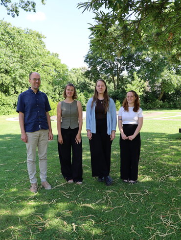 Ein Professor und drei Studentinnen stehen im Park.
