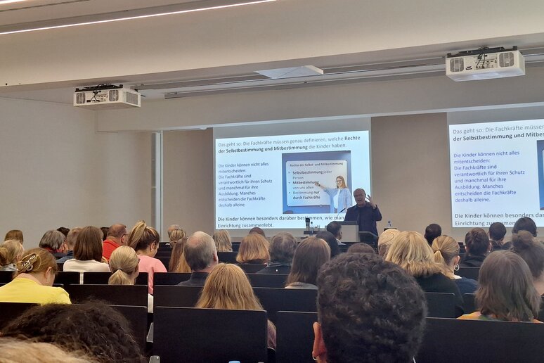 Prof. i. R. Dr. Benedikt Sturzenhecker steht am Rederpult und erklärt, wie man Kinderrechte und Partizipation in Einrichtungen konkret macht.