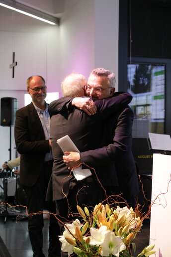 Zwei Männer umarmen den Redner als Dankeschön für die Rede.