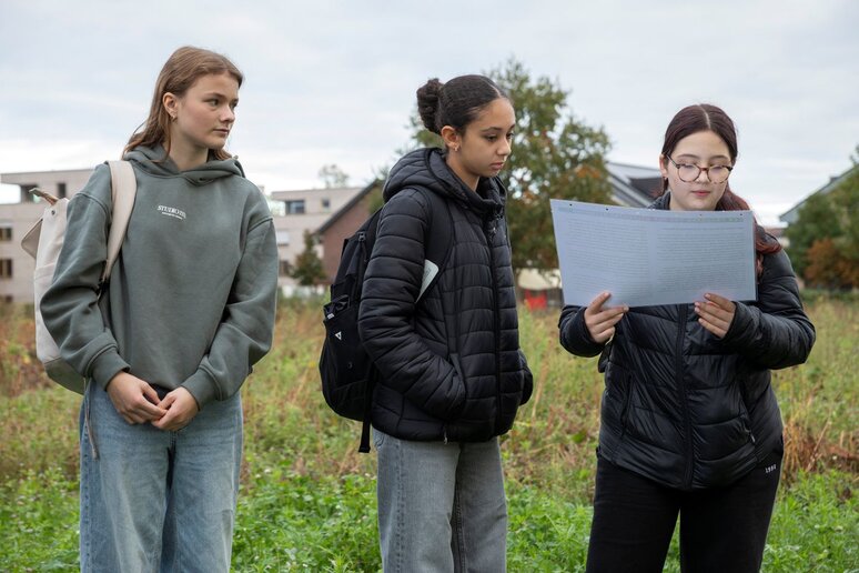 Drei Schülerinnen in der Natur stehen nebeneinander. Eine hält eine große Karte in der Hand.