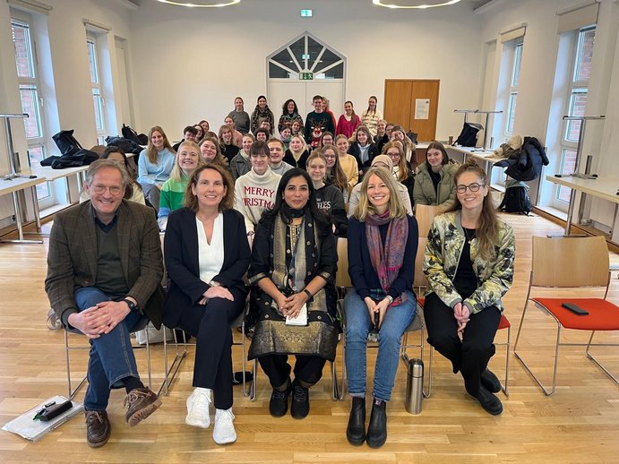 Es wird ein Hörsaal des katho-Standorts Münster mit Gruppenfoto von Studierenden und 5 Prüfessor_innen gezeigt.