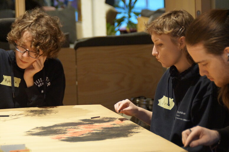 Schüler:innen sitzen am Tisch und gestalten Bilder.