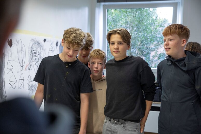 Schüler schauen sich die mit Kohle gemalten Bilder der Mitschüler:innen an.