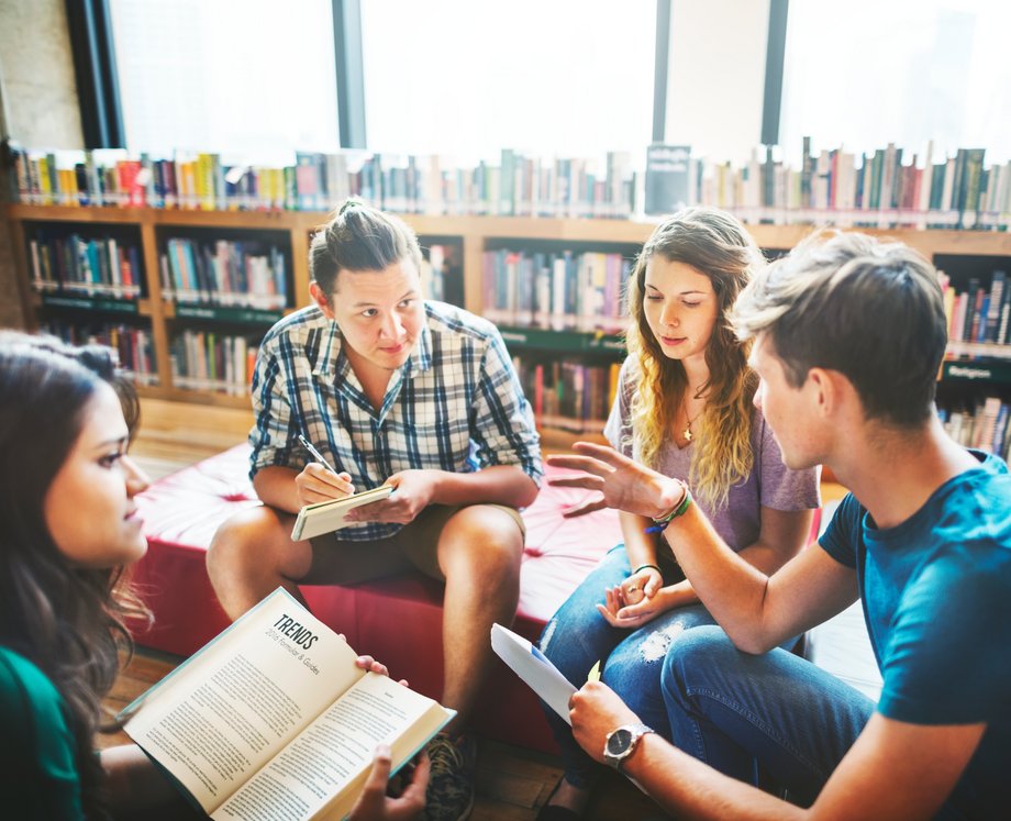 Eine Gruppe von vier Studierende unterhält sich angeregt in einer Bibliothek. 