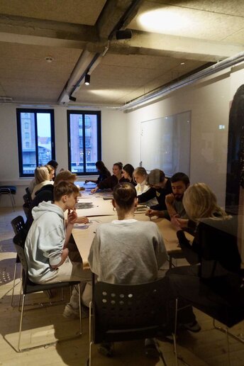 Schüler:innen sitzen an einen Tisch und arbeiten an Bildern.