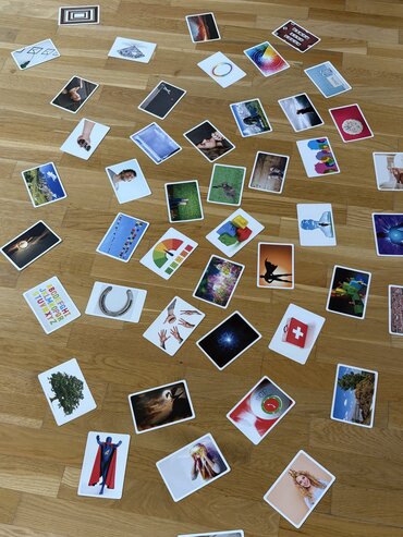Auf einem Holzboden verteilt liegen bunte Bildkarten.