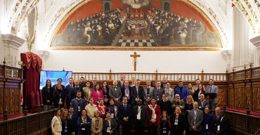 Gruppenfoto einer großen Gruppe von Personen in einem historischen Raum mit bemaltem Deckengewölbe und einem Kreuz an der Wand.
