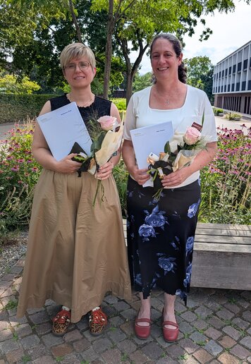 Die Absolvent_innen stehen mit ihrem Zeugnis unter einem Baum und lächeln in die Kamera.