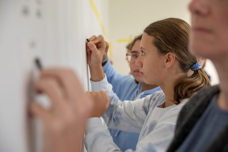 Drei Schüler:innen schreiben etwas auf eine Tafel.