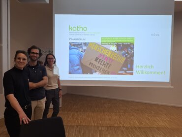 Drei Personen stehen links vor einer Leinwand, auf der der Veranstaltungstitel "Menschenrechte statt rechte Menschen" projiziert ist.