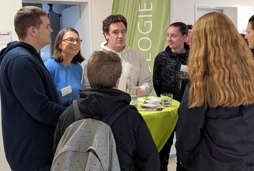 katho-Studierende und Studieninteressierte stehen an einem runden Tisch und unterhalten sich. Die Personen sehen fröhlich aus.