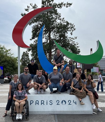 Das gesamte Team steht um das offizielle Paralympics Symbol verteilt und jubelt in die Kamera.